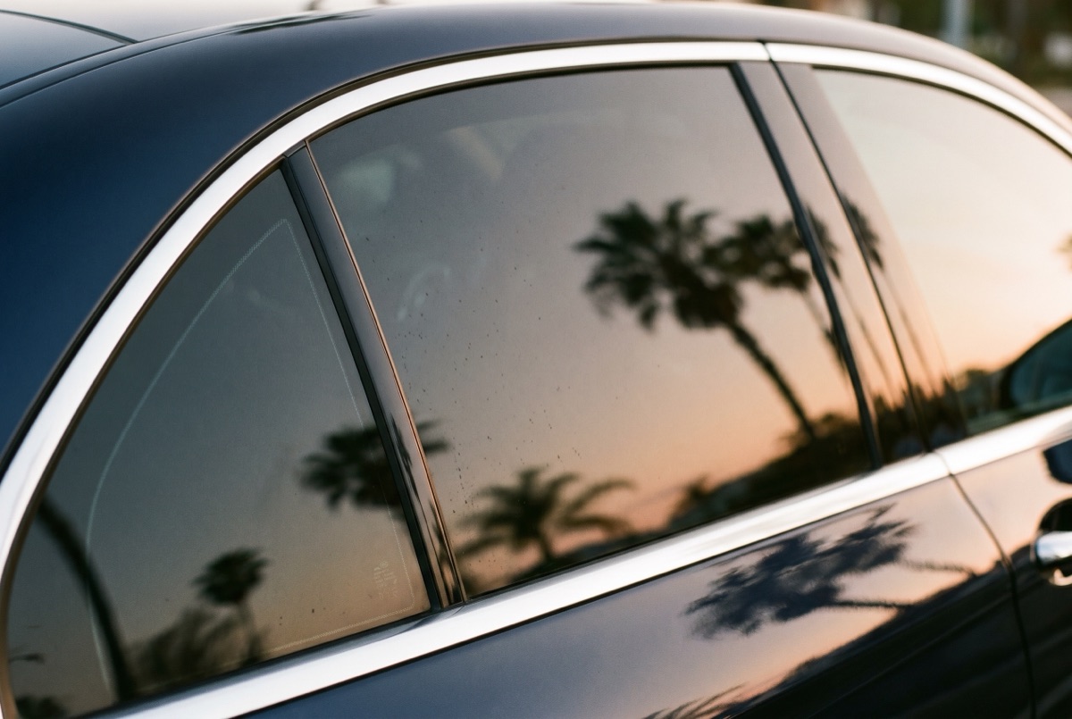 A car's rear windows with dark ceramic IR heat-rejection tint installed, reflecting palms at golden hour